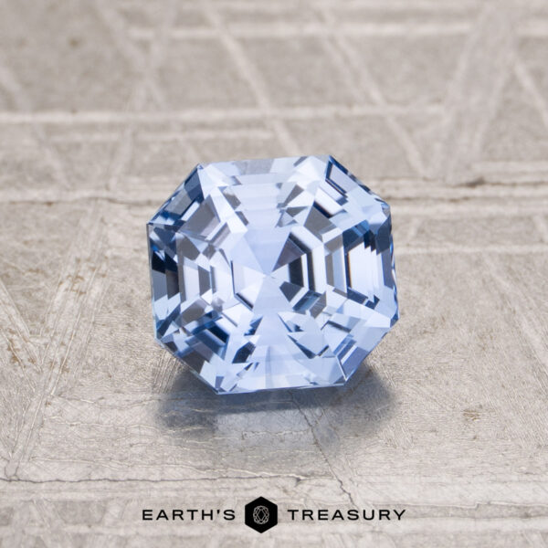 1.55-Carat Sky Blue Ceylon Sapphire The 1.55-Carat Ceylon Sapphire, a faceted octagonal blue gemstone, is displayed on a textured metallic surface with "EARTH'S TREASURY" at the bottom.
