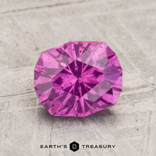 1.91-Carat Pastel Pyrope Garnet A faceted 1.91-Carat Pastel Pyrope Garnet with internal inclusions rests on a textured, light surface. "EARTH'S TREASURY" is printed at the bottom.