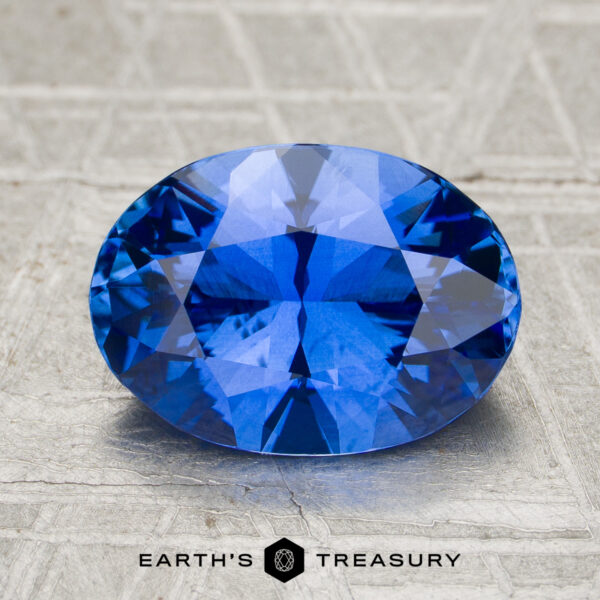 3.07-Carat Ceylon Sapphire (Heated) A 3.07-carat heated Ceylon sapphire, oval-cut and blue, displayed on a textured surface with "Earth's Treasury" written below.