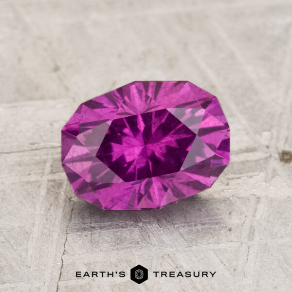 1.83-Carat Pastel Pyrope Garnet A 1.83-carat Pastel Pyrope Garnet, faceted in an oval shape, rests on a textured light surface with "EARTH'S TREASURY" below it.