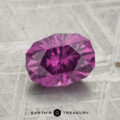 A 1.83-carat pastel pyrope garnet is displayed on a textured gray surface with "EARTH'S TREASURY" at the bottom.