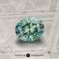 A 1.14-carat Montana sapphire gemstone, faceted in an oval shape and teal in color, is displayed on a textured gray surface with the Earth's Treasury logo beneath it.
