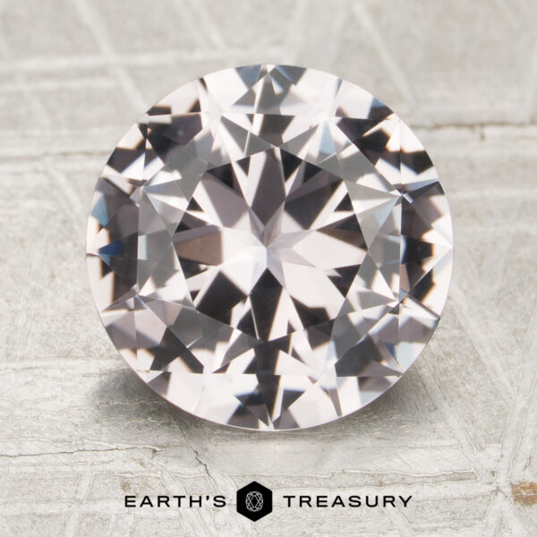 3.48-Carat Sapphire A 3.48-carat round brilliant-cut sapphire is displayed on a light, patterned surface with the text "Earth's Treasury" and a logo beneath it.