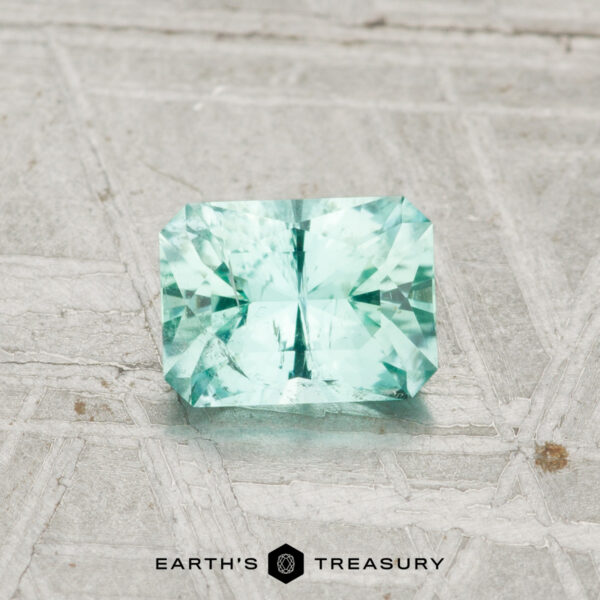0.69-Carat Maine Tourmaline A 0.69-carat Maine tourmaline, rectangular and faceted in light blue-green, is shown on a textured gray background with "Earth's Treasury" visible below.