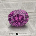 A 1.75-carat pastel pyrope garnet, cut in a faceted oval shape, rests on a textured gray surface with "EARTH'S TREASURY" at the bottom.