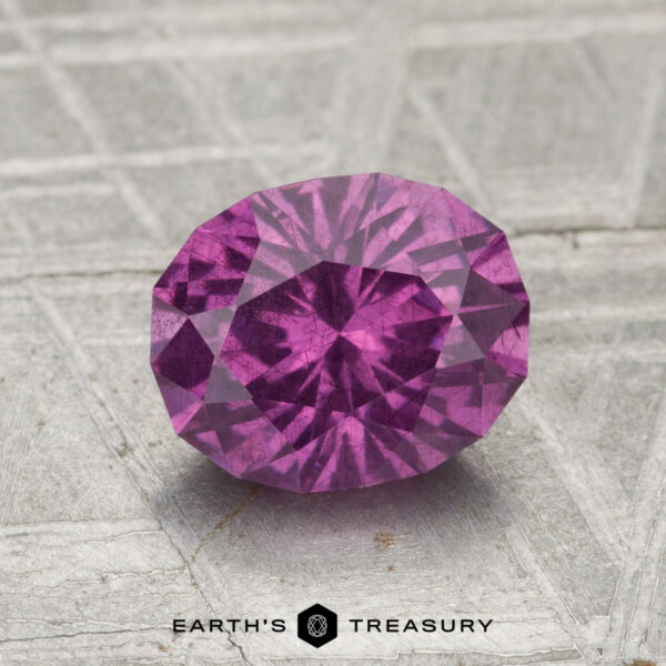 1.75-Carat Pastel Pyrope Garnet A 1.75-carat pastel pyrope garnet, cut in a faceted oval shape, rests on a textured gray surface with "EARTH'S TREASURY" at the bottom.
