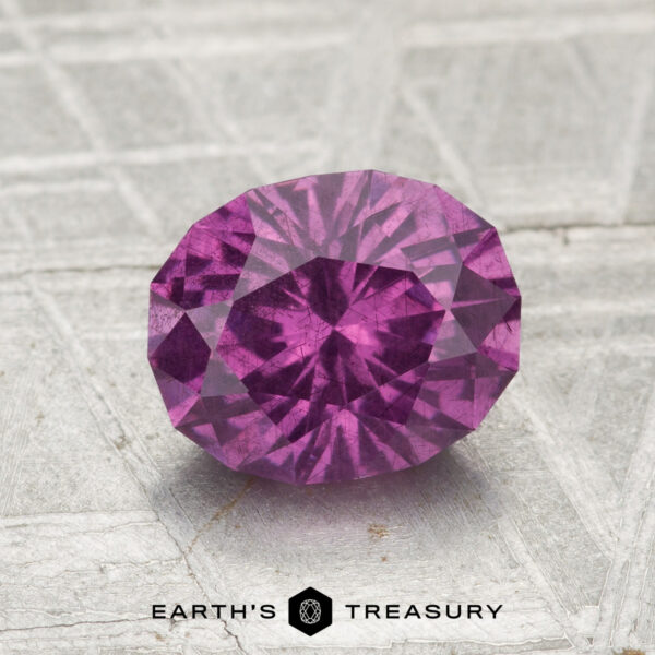 1.75-Carat Pastel Pyrope Garnet A 1.75-carat pastel pyrope garnet, cut in a faceted oval shape, rests on a textured gray surface with "EARTH'S TREASURY" at the bottom.