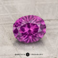 A 1.75-carat pastel pyrope garnet with an oval cut rests on a textured, light surface, featuring the text "EARTH'S TREASURY" at the bottom.