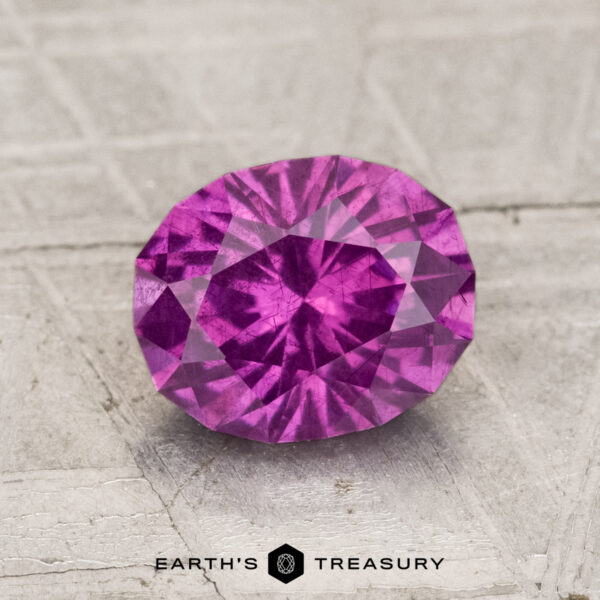 1.75-Carat Pastel Pyrope Garnet A 1.75-carat pastel pyrope garnet with an oval cut rests on a textured, light surface, featuring the text "EARTH'S TREASURY" at the bottom.