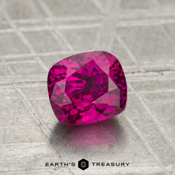 1.41-Carat Ruby (Heated) A cushion-cut, vivid pink 1.41-carat ruby (heated) rests on a textured metallic surface, with the "EARTH'S TREASURY" logo and text displayed at the bottom.
