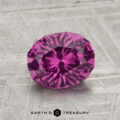 A 1.71-carat pastel pyrope garnet with inclusions, oval-cut and purple in color, rests on a textured gray surface with the Earth’s Treasury logo at the bottom.