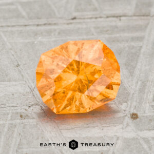 1.96-carat Spessartine Garnet displayed on a textured gray surface, with "Earth's Treasury" text at the bottom.