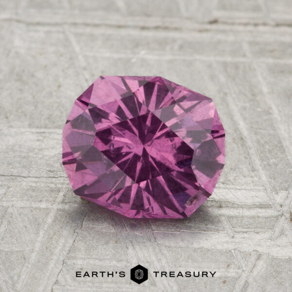 1.71-Carat Pastel Pyrope Garnet A 1.71-carat pastel pyrope garnet, faceted and round, is displayed on a textured gray surface with "Earth's Treasury" branding below.