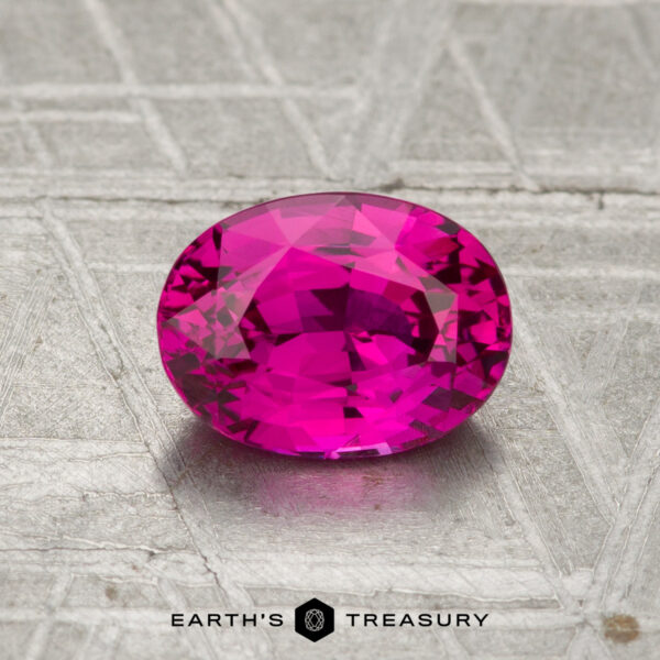 1.29-Carat Vietnam Ruby (Heated) A 1.29-carat Vietnamese Ruby (heated), faceted oval and pink, rests on a textured metallic surface with "Earth's Treasury" below.