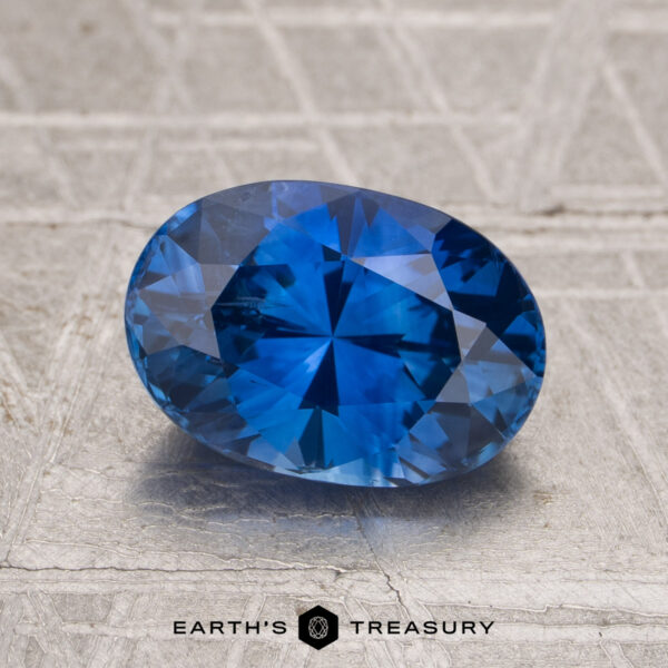 2.42-Carat Ceylon Sapphire (Heated) 2.42-Carat Ceylon Sapphire (Heated) in oval cut shown on a textured gray surface, featuring the "Earth's Treasury" logo and text at the bottom.