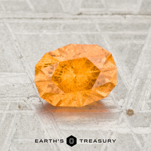 1.66-Carat Spessartine Garnet A 1.66-carat Spessartine Garnet with orange facets sits on a textured grey surface, displaying the "EARTH'S TREASURY" logo below.