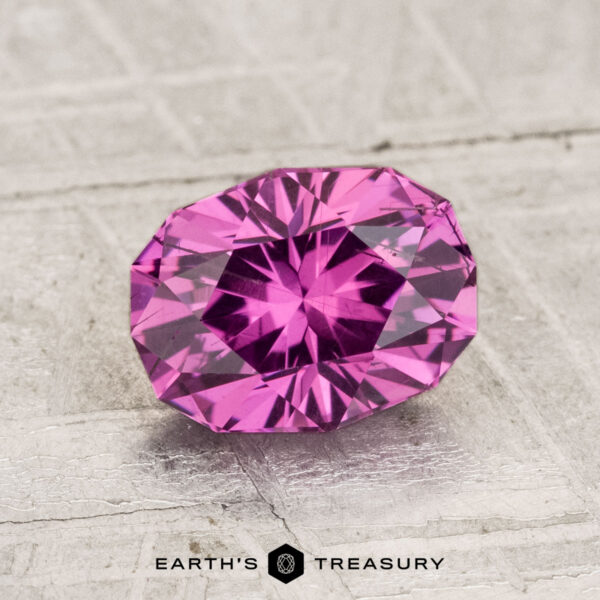 1.70-Carat Pastel Pyrope Garnet A 1.70-carat pastel pyrope garnet, faceted in an oval shape, is displayed on a light textured surface with "Earth's Treasury" and a small logo at the bottom.