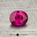 0.98-carat oval-cut vivid pink-red Ceylon Ruby (heated) displayed on a textured gray surface, with "Earth's Treasury" logo and text at the bottom.