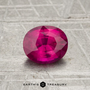 0.98-carat oval-cut vivid pink-red Ceylon Ruby (heated) displayed on a textured gray surface, with "Earth's Treasury" logo and text at the bottom.