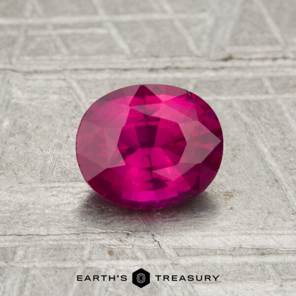 0.98-Carat Ceylon Ruby (Heated) 0.98-carat oval-cut vivid pink-red Ceylon Ruby (heated) displayed on a textured gray surface, with "Earth's Treasury" logo and text at the bottom.