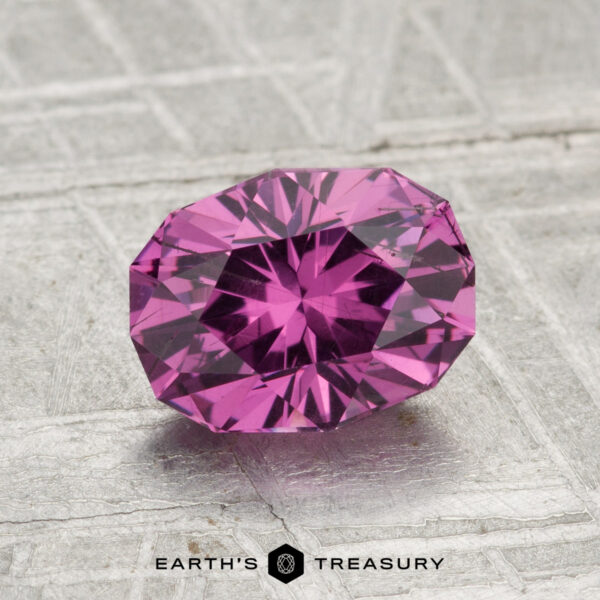 1.70-Carat Pastel Pyrope Garnet A 1.70-carat pastel pyrope garnet with an oval cut rests on a textured metallic surface, "EARTH'S TREASURY" visible beneath.