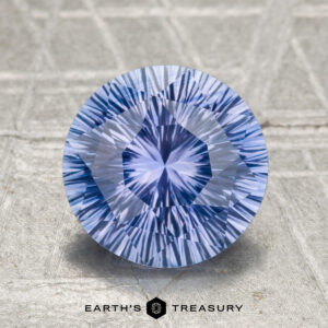 A 2.04-carat heated Ceylon sapphire, round and intricately faceted, is displayed on a textured surface with the "Earth’s Treasury" logo beneath it.