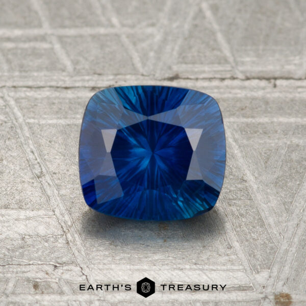 1.17-Carat Ceylon Sapphire (Heated) A 1.17-carat heated Ceylon sapphire with a cushion cut is displayed on a textured metallic surface, featuring the "EARTH'S TREASURY" logo and text at the bottom.