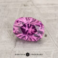 A 1.38-carat pastel pyrope garnet gemstone is shown on a gray textured surface, featuring the "EARTH'S TREASURY" logo and text at the bottom.