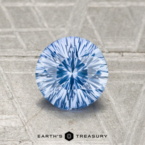 1.05-Carat Ceylon Sapphire A round, blue faceted 1.05-carat Ceylon Sapphire with a starburst pattern is displayed on a textured metallic surface above the text "EARTH'S TREASURY.