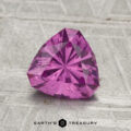 A 1.34-carat pastel pink pyrope garnet, faceted in a heart shape, rests on a textured gray surface with “EARTH'S TREASURY” displayed at the bottom.