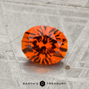 A 1.37-carat Spessartine Garnet, expertly faceted in an oval cut, is shown on a metallic patterned surface with "EARTH'S TREASURY" at the bottom.