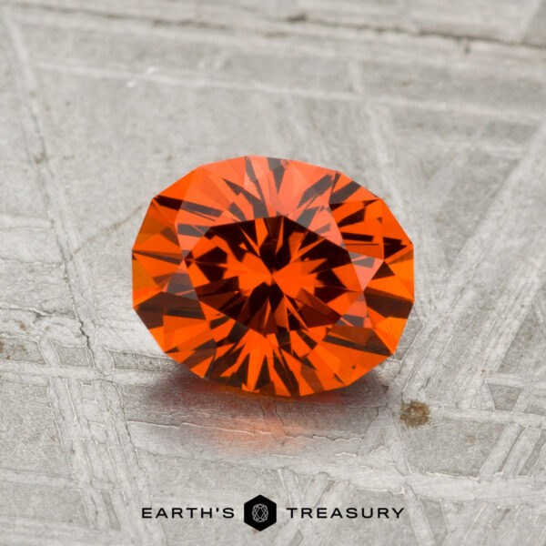 1.37-Carat Spessartine Garnet A 1.37-carat Spessartine Garnet, expertly faceted in an oval cut, is shown on a metallic patterned surface with "EARTH'S TREASURY" at the bottom.