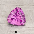 A 1.34-carat pastel pyrope garnet, trilliant-cut in vivid pink, is displayed on a light textured surface with "Earth's Treasury" at the bottom.