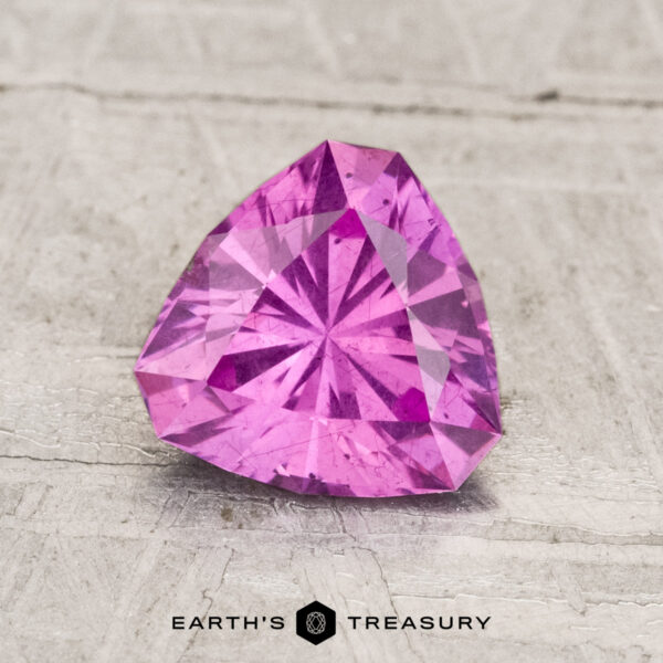 1.34-Carat Pastel Pyrope Garnet A 1.34-carat pastel pyrope garnet, trilliant-cut in vivid pink, is displayed on a light textured surface with "Earth's Treasury" at the bottom.
