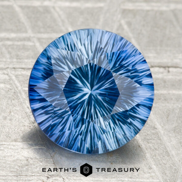 2.99-Carat Ceylon Sapphire (Heated) A 2.99-carat round Ceylon sapphire (heated), blue with intricate internal patterns, is displayed on a textured gray surface. "Earth's Treasury" appears as logo text at the bottom.