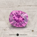 A 1.19-carat pastel pyrope garnet, round brilliant-cut, is displayed on a textured light surface with "EARTH'S TREASURY" at the bottom.
