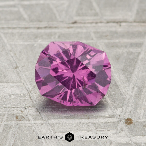 1.19-Carat Pastel Pyrope Garnet A 1.19-carat pastel pyrope garnet gemstone rests on a textured gray surface with “EARTH’S TREASURY” and a hexagonal logo below.