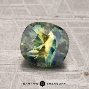 A 2.14-carat sapphire with green and yellow hues sits on a textured surface, with "EARTH'S TREASURY" displayed below.