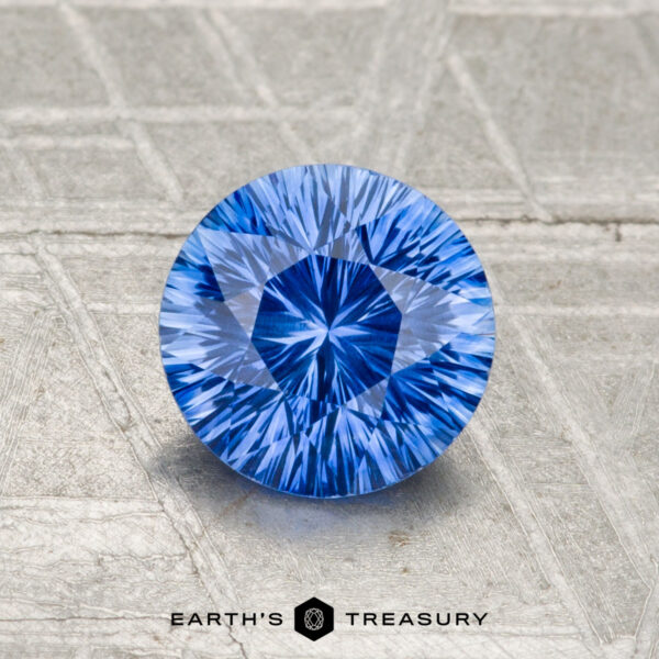 1.15-Carat Ceylon Sapphire (Heated) A 1.15-carat, round brilliant-cut Ceylon sapphire (heated) is showcased on a textured, light-colored surface with "EARTH'S TREASURY" at the bottom.
