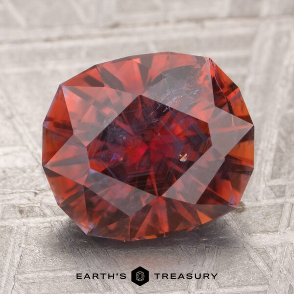 4.18-Carat Montana Sapphire (Heated) A 4.18-carat heated Montana sapphire, deep red with visible inclusions, rests on a textured metallic surface. "EARTH'S TREASURY" appears at the bottom.