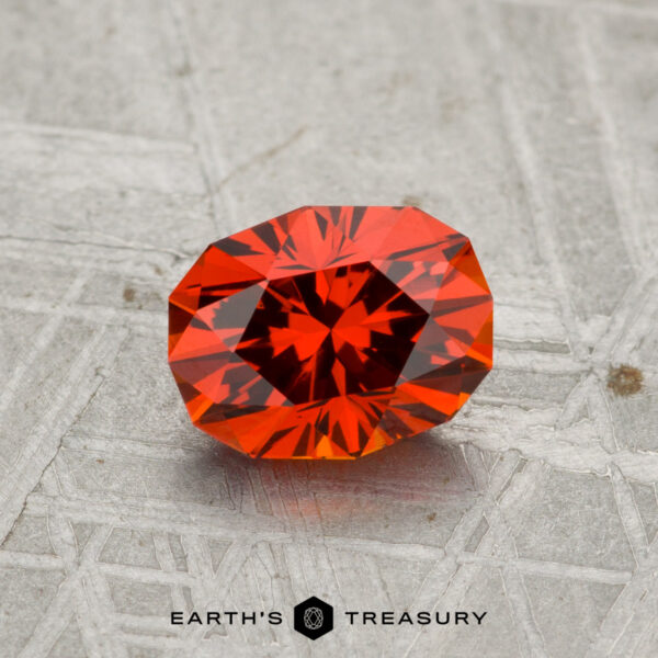 1.17-Carat Spessartine Garnet A 1.17-carat Spessartine garnet, expertly faceted in an oval cut, rests on a textured grey surface with "Earth's Treasury" displayed below.