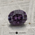 A 1.46-carat color-change garnet, faceted in an oval cut, sits on a textured gray surface with "Earth's Treasury" written below.