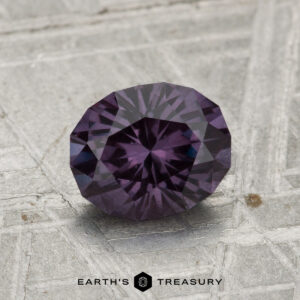 A 1.46-carat color-change garnet, faceted in an oval cut, sits on a textured gray surface with "Earth's Treasury" written below.