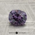 A faceted, round 1.21-carat color-change garnet is displayed on a textured gray surface with the text "EARTH'S TREASURY" at the bottom.