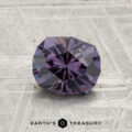 A faceted, round 1.21-carat color-change garnet is displayed on a textured gray surface with the text "EARTH'S TREASURY" at the bottom.