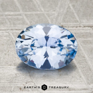 A 1.58-carat Ceylon sapphire in an oval cut rests on a textured grey surface with "Earth's Treasury" beneath it.