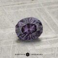A 0.81-carat color-change garnet, faceted in an oval shape with a deep purple hue, is showcased on a textured gray surface, featuring the "EARTH’S TREASURY" text at the bottom.