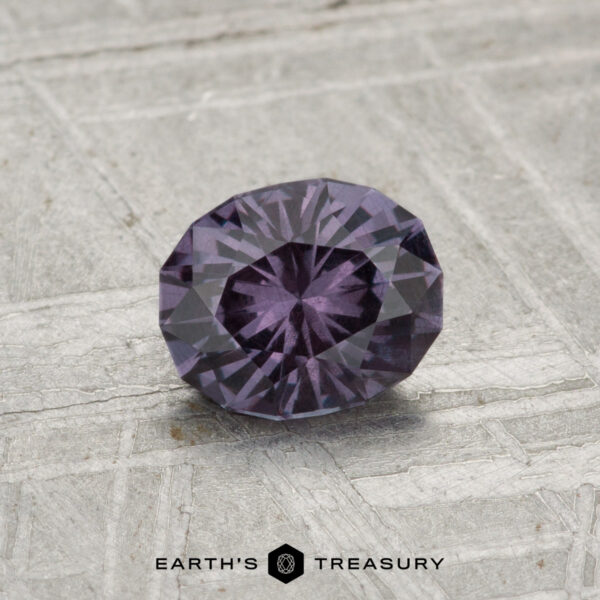 0.81-Carat Color-Change Garnet A 0.81-carat color-change garnet, faceted in an oval shape with a deep purple hue, is showcased on a textured gray surface, featuring the "EARTH’S TREASURY" text at the bottom.