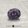 A 0.81-carat color-change garnet, faceted in an oval shape with a deep purple hue, is showcased on a textured gray surface, featuring the "EARTH’S TREASURY" text at the bottom.