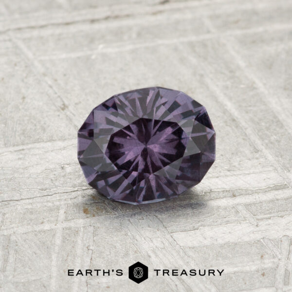 0.81-Carat Color-Change Garnet A 0.81-carat color-change garnet, faceted in an oval shape with a deep purple hue, is showcased on a textured gray surface, featuring the "EARTH’S TREASURY" text at the bottom.
